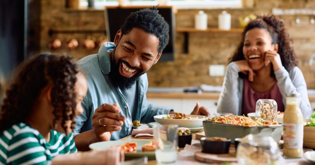 This image shows a happy family of three sitting at the table eating a meal together.