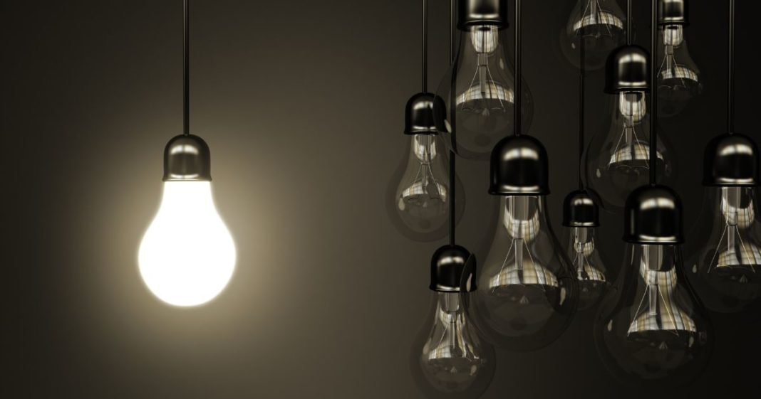 This image shows a group of hanging light bulbs that are turned off next to one that is turned on.