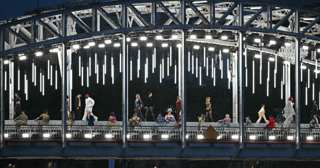 Models present creations while walking a catwalk erected along the Passerelle Debilly bridge as the boat carrying the delegations of Romania and Rwanda sails underneath along the Seine river during the opening ceremony of the Paris 2024 Olympic Games in Paris on July 26, 2024.