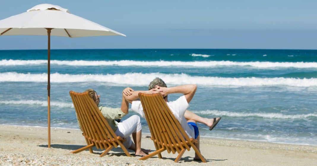 This image shows a retired couple sitting in chairs next to an umbrella on the beach.