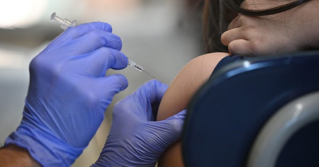 A little girl comforts her sister by placing her hand on her sister's neck as a nurse prepares to administer a pediatric dose of Covid-19 vaccine.