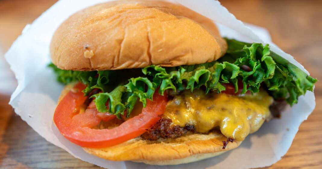 Close-up of a cheeseburger with tomato and lettuce in a paper wrapper at Shake Shack, Walnut Creek, California, August 25, 2024.